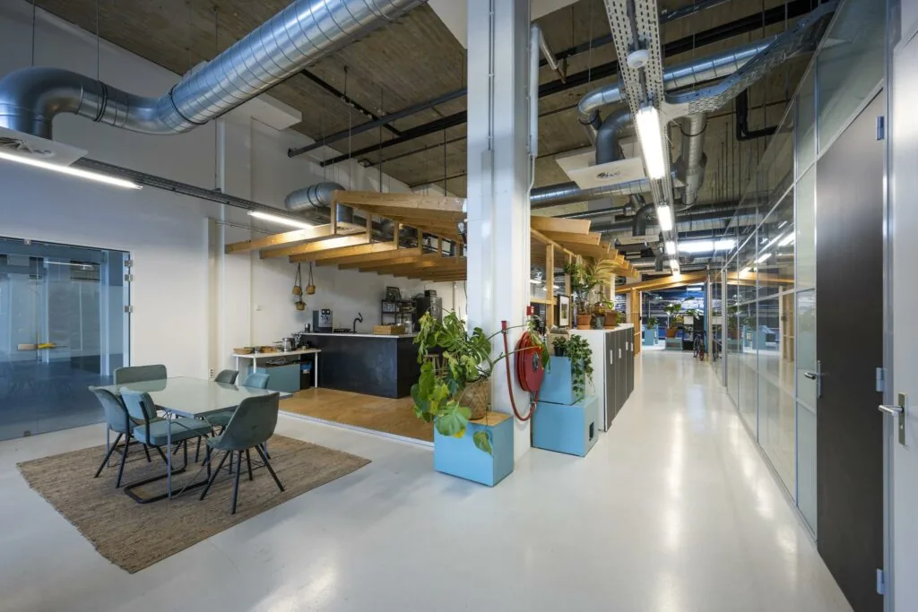 Moderne kantoorruimte aan de Joan Muyskenweg met open keuken, zithoek en industriële plafondleidingen.